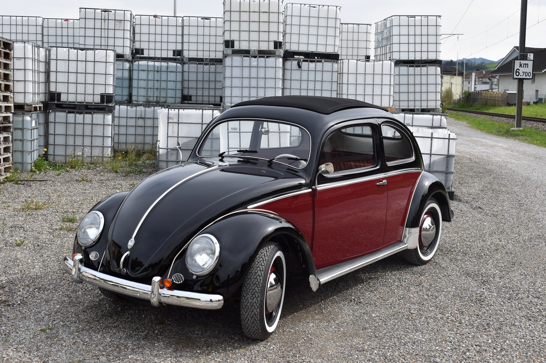 Schwarz roter VW Käfer Ovali Beetle Bug Typ 1 aus dem Jahre 1953 mit Faltdach in Seitenansicht vor Plastikcontainer mit Kiessplit