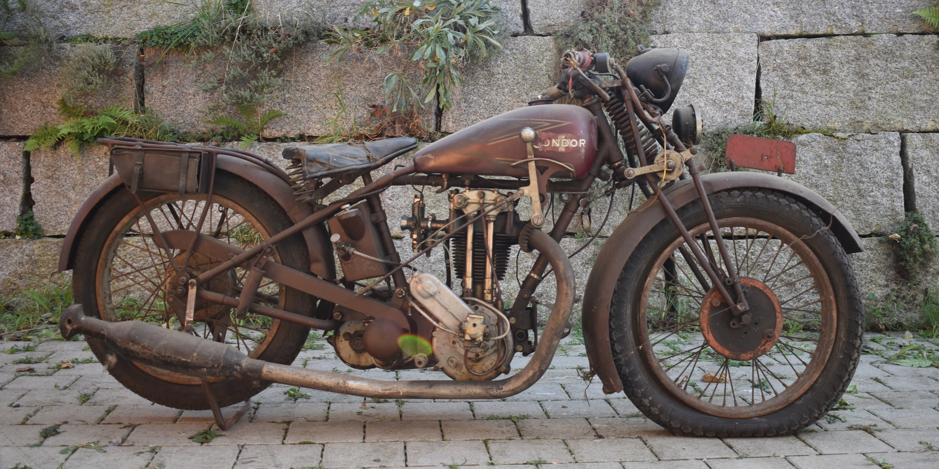 Seitenansicht eines braunen Condor Grand Sport 512 Motorrads aus dem Jahre 1929 mit einer Steinmauer im Hintergrund